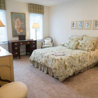 A cozy bedroom featuring a floral bedspread, wooden desk, and plush carpeting.