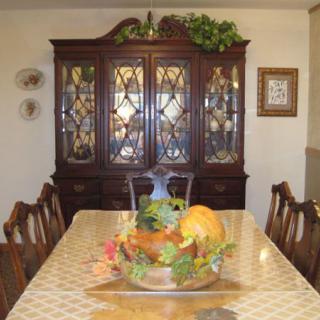 A dining room with a wooden table, ornate china cabinet, and a decorative autumn-themed centerpiece.