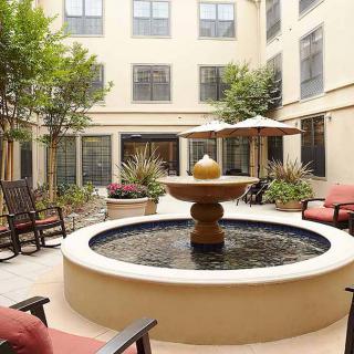 A serene courtyard with a central fountain, surrounded by outdoor seating and shaded by umbrellas.