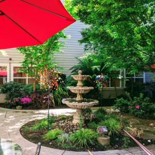 A beautifully landscaped garden patio with a central fountain and a red umbrella providing shade.