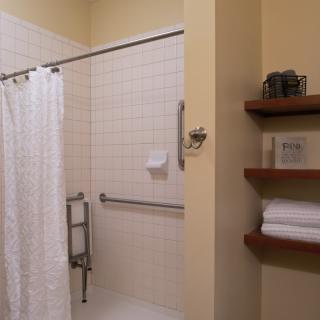A clean and organized bathroom with a shower, equipped with grab bars and neatly arranged towels on shelves.