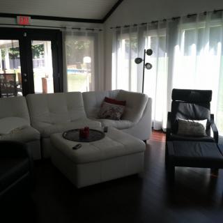 A cozy living room with a white sectional sofa and large windows letting in natural light.