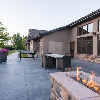 A modern outdoor patio area with a fire pit and furniture, set against a landscaped garden.