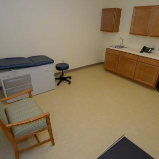 A small medical examination room with an exam table, chair, and cabinets.