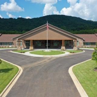 A scenic view of a large building with a driveway, set against a backdrop of mountains and a partly cloudy sky.