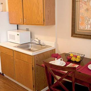 A cozy kitchen and dining area with wooden cabinets, a microwave, a sink, and a small table set for two.