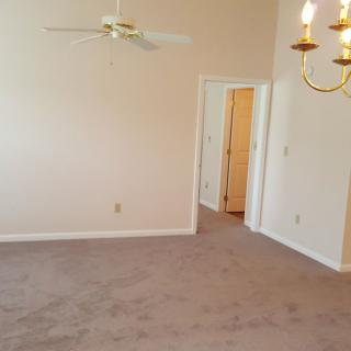 An empty room with beige walls, carpet flooring, a ceiling fan, and a chandelier.