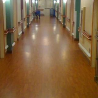 A well-lit hospital corridor with handrails and wooden flooring.