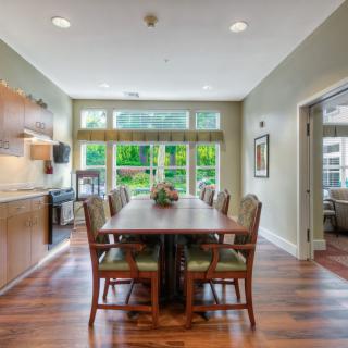A modern dining room with a long table and chairs, featuring wood flooring and abundant natural light.