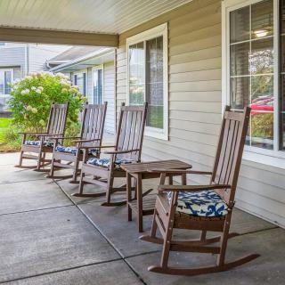 A cozy porch with four wooden rocking chairs, each adorned with patterned cushions, situated outside a home.