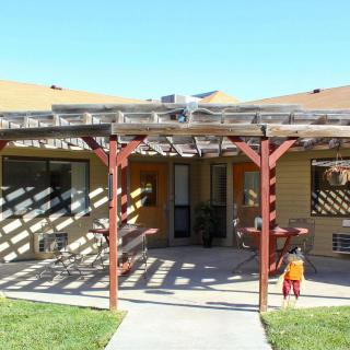A sunny day in the backyard featuring a house with a pergola and a child playing.