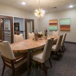 A modern dining or conference room with a large wooden table, beige upholstered chairs, and contemporary artwork on the walls.