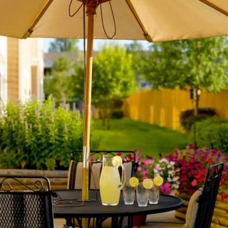 A sunny patio setup with a table under an umbrella, featuring a pitcher of lemonade and glasses ready for a refreshing drink.