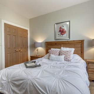A cozy bedroom featuring a neatly made bed with white bedding, flanked by wooden nightstands and modern lamps.