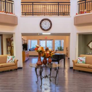A spacious living area featuring elegant furniture, decorative vases with flowers, and a prominent wall clock.