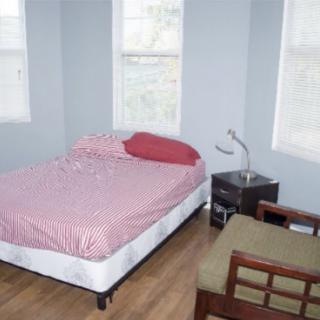 A minimalist bedroom with a bed, nightstand, and chair by the windows.