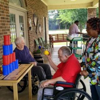 Elderly individuals in wheelchairs engaging in an outdoor activity with colorful cups.