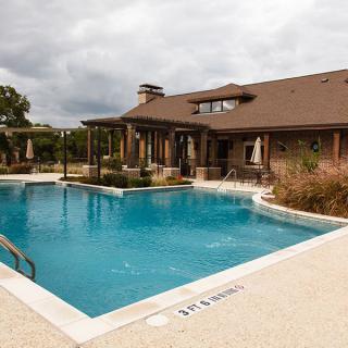 A residential outdoor swimming pool with a patio and house in the background.
