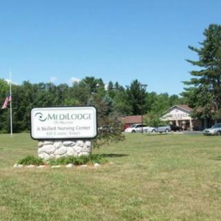 A scenic view of a building with a sign in front, surrounded by grass and trees under a clear blue sky.
