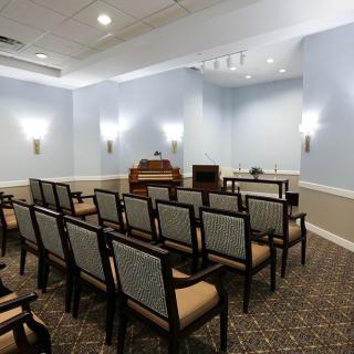 An empty chapel with rows of chairs facing an organ and altar, softly lit by wall sconces.