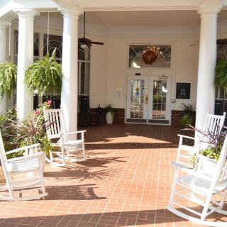A welcoming front porch with white rocking chairs and lush green plants.