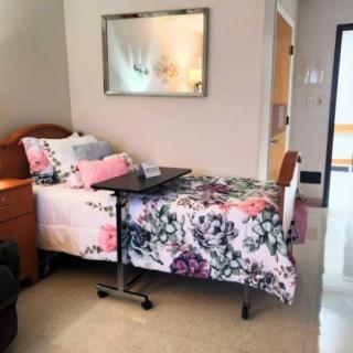 A well-decorated hospital room with a floral-themed single bed and an overbed table.