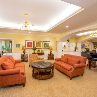 A warmly lit living room featuring two orange sofas, a central coffee table, decorative plants, and framed artwork on the walls.