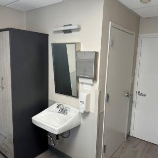 A clean and modern bathroom setup featuring a sink, mirror, hand dryer, and storage cabinet.