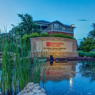 A scenic view of a building with a sign, surrounded by nature and reflected in a pond.