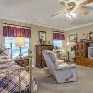 A cozy bedroom with a ceiling fan, featuring a bed, recliner, and television in a warm setting.