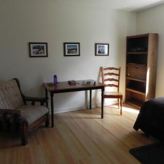 A minimalist room featuring a table, chairs, and a bookshelf with framed pictures on the wall.