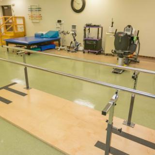 A rehabilitation room equipped with parallel bars and various exercise machines for physical therapy.