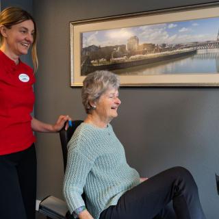 A healthcare worker assists an elderly woman with seated exercises in a comfortable setting.