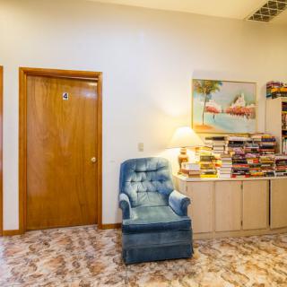 A cozy living room corner featuring a blue armchair, bookshelf, and a lamp under a painting.