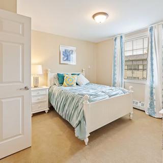 A cozy bedroom with a neatly made bed, nightstand, and soft light filtering through the curtains.
