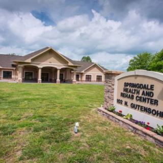 A health and rehab center building with a sign in the foreground and a lawn under a partly cloudy sky.