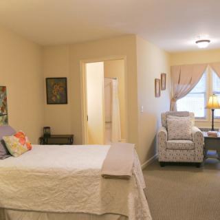 A cozy bedroom interior with a bed, chair, and window letting in natural light.