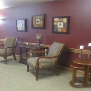 A well-decorated lobby area featuring comfortable chairs, a side table, and framed artwork on a maroon wall.