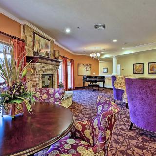 A cozy living room featuring a stone fireplace, a piano, and vibrant purple seating.