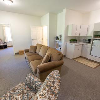 Cozy apartment interior featuring a living room with a sofa and armchair, adjacent to a compact kitchen area.
