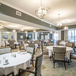 An elegant dining room with round tables and chandeliers, set for guests.