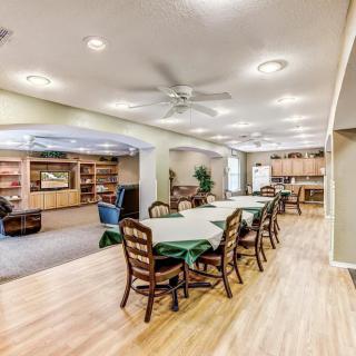 A spacious dining area with tables and chairs in an open layout, featuring a wooden floor and ceiling fans.