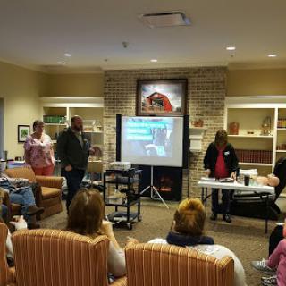 A community health workshop in progress, with a presenter demonstrating techniques to an engaged audience.