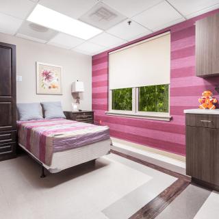 A modern hospital room with pink striped walls and a single bed.
