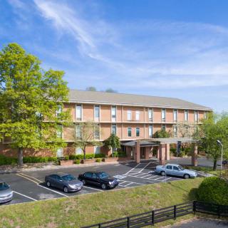 A hotel with a parking lot and surrounding trees under a clear blue sky.