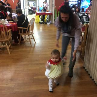 A child playfully waddles along as an adult assists in a lively dining environment.