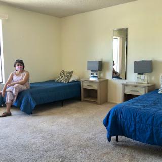 A spacious bedroom featuring two beds, a mirror, and a person sitting on one of the beds.