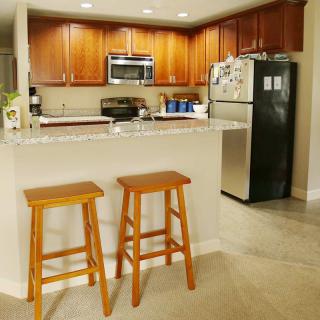 A modern kitchen with wooden cabinets, stainless steel appliances, and two bar stools at a countertop.