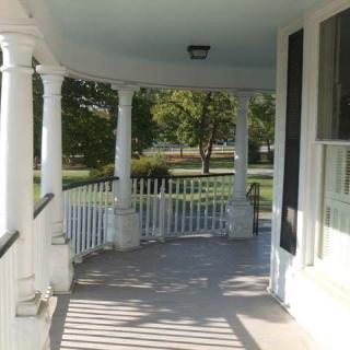 A sunny porch with white columns overlooking a garden.