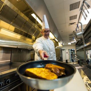 A professional chef cooking in a modern kitchen, preparing toast in a frying pan.